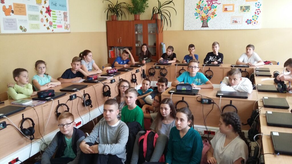 Uczniowie siedzą przy biurkach w sali do informatyki