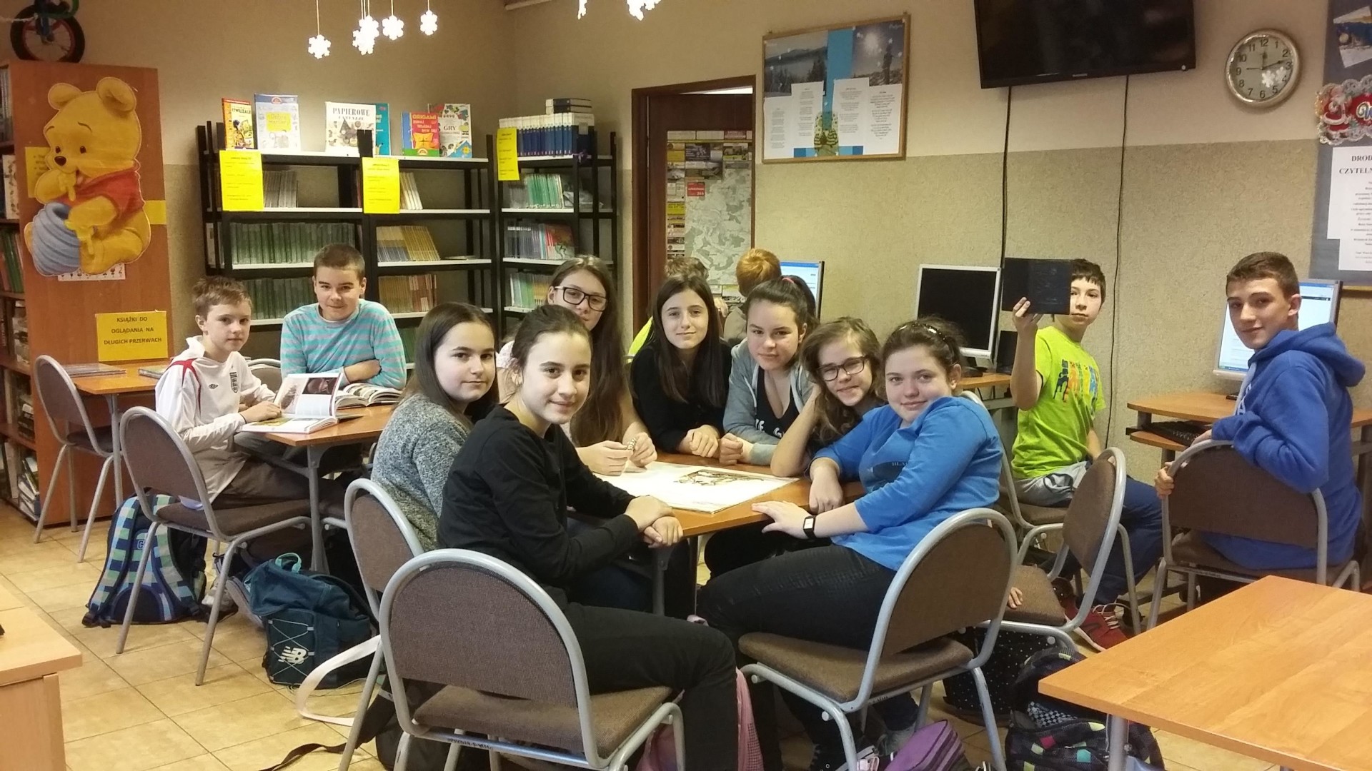 Zajęcia w bibliotece - uczniowie siedzą przy stolikach, na których leżą otwarte książki